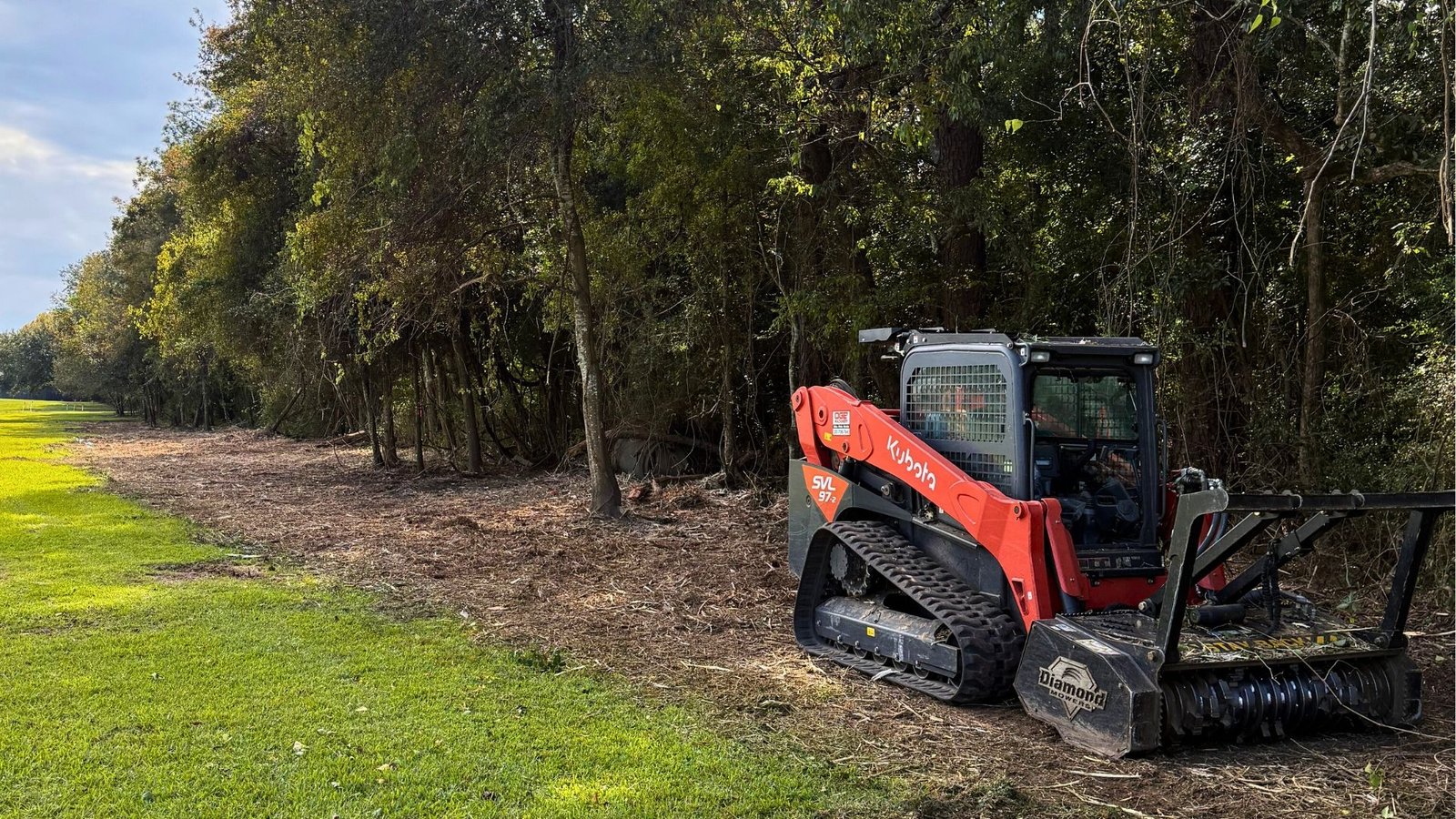 skid steer cutting brush around a fence line